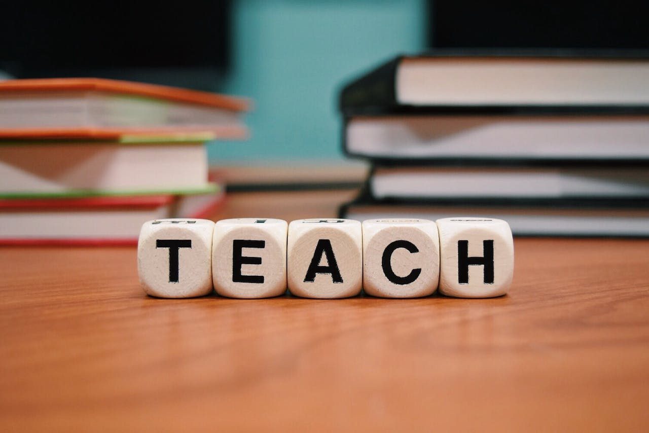 Books on a table with the word teach spelled out with beads